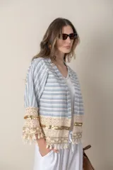 Chaqueta corta de jean rayada en tonos celeste y blanco, con apliques de puntilla y flecos en ruedo y mangas.
