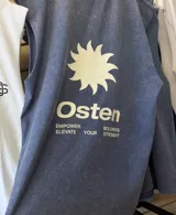 Musculosa sin mangas, color azul oscuro con efecto acid wash o teñido desgastado. Presenta un estampado frontal minimalista en blanco con un sol estilizado y la palabra "Osten".