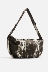 Bolso de hombro tipo bandolera, confeccionado en tejido de algodón con estampado abstracto en tonos blanco y negro. Cuenta con un compartimento principal con cierre de cremallera, un bolsillo interior con cremallera y asa de hombro ajustable.