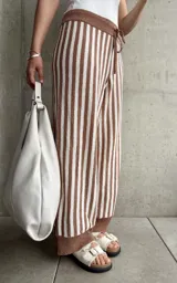 Pantalón tejido a rayas verticales color marrón y blanco, con cintura y tobillos acanalados con cordón ajustable.