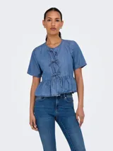 Camisa de denim celeste con lazo. Diseño de cuello camisero, mangas cortas tipo box y calce regular. Incluye detalle de lazo y recorte en la cintura.