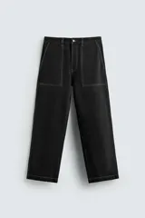 Pantalón relaxed fit de denim negro con costuras blancas en contraste, bolsillos frontales y traseros de parche, cierre frontal con cremallera y botón.