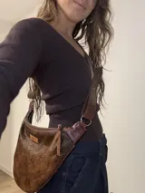 Cartera bandolera de cuero con pelo animal print marrón y blanco, correa de cuero ajustable con hebilla y cierre con cremallera.