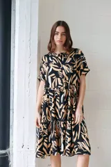 Vestido camisero midi con volados, estampado con hojas en tonos camel, blanco y negro. Tiene cuello redondo, mangas cortas y cierre frontal con botones.