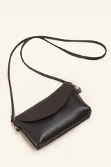 Cartera tipo sobre de cuero vacuno, con solapa frontal, cierre y broche magnético. Incluye correa larga ajustable y extraíble para usar como bandolera.