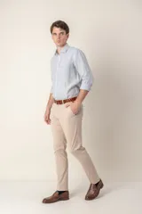 Pantalón de vestir color gris claro, de corte slim fit, con bolsillos laterales y traseros. Se ajusta a la cintura con cinturón de cuero marrón.