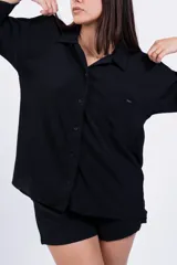 Camisa negra de corte amplio, con cuello clásico, cierre frontal con botones, manga larga con puños arremangados y bolsillo de parche en el pecho.