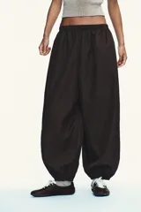 Pantalón bombacho marrón de nylon con cintura elástica, bolsillos laterales ocultos y bajo abullonado con elástico.