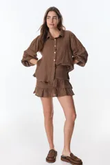 Camisa celeste de lino con cuello clásico, abotonada al frente y mangas largas con detalle de puntilla en los hombros.