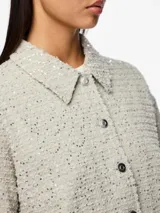Chaqueta color crema con lentejuelas plateadas, cuello camisero, cierre frontal con botones y mangas largas. Marca Pieces.