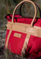 Bolso de playa rojo de lona con detalles en cuero color beige, doble asa de mano y logo de la marca en el frente.