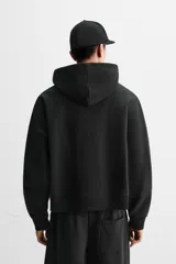 Sudadera negra corta con capucha, manga larga, bolsillo tipo canguro y terminaciones en rib.