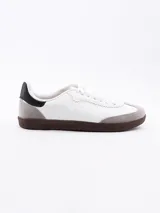 Zapatillas deportivas blancas con puntera de gamuza gris, talón negro y suela marrón.