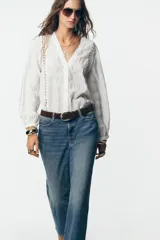 Blusa blanca de manga larga con escote en pico, detalle de tejido con frunces, entredoses y plumeti. Cierre frontal con botones.