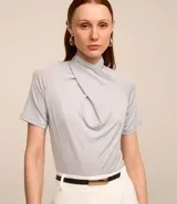 Blusa color gris claro con detalle drapeado en el cuello y mangas cortas.