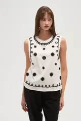 Musculosa blanca de algodón con cuello redondo y breteles anchos. Presenta apliques bordados en negro con motivos florales y geométricos. Corte al cuerpo.