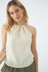 Blusa sin mangas color crudo, con cuello halter y cordón ajustable.