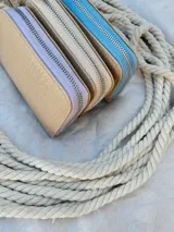 Billetera pequeña de cuero color beige con textura croco, forrada, con cierre metálico y pulsera de cuero.