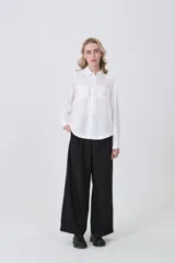 Camisa blanca de manga larga con cuello clásico, dos bolsillos frontales con tapa y botones a presión. Presenta un tejido con textura sutil de rayas verticales.