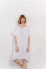 Vestido corto blanco de lino, con corte recto y calce relajado. Presenta botones de madera decorativos en los laterales.