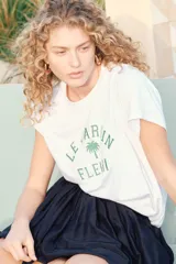 Remera blanca de algodón con corte amplio, cuello redondo y mangas cortas. Estampado frontal con texto en francés "Le Jardin Fleuri" y una palmera.