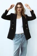 Blazer color blanco hueso, de corte entallado y doble botonadura dorada.