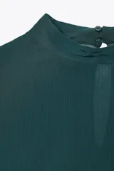 Camisa verde esmeralda de cuello alto y manga larga con volantes en los puños. Cierre en la espalda con abertura y botones.
