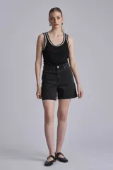 Remera negra ajustada al cuerpo, tipo musculosa, con escote redondo y ribetes en blanco con apliques de perlas en el contorno del cuello y las sisas.