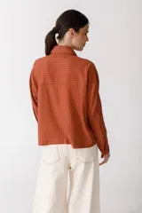 Blusa blanca de lino con cuello polo, manga larga y botones dorados. Presenta costuras a contratono en color naranja.