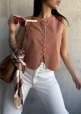 Chaleco color terracota con botones frontales y corte irregular en el ruedo. Sin mangas y con cuello redondo.