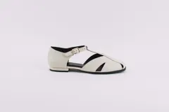 Zapato flat de cuero color crema, con puntera cerrada y aberturas laterales. Tiene una tira con hebilla sobre el empeine y suela plana.