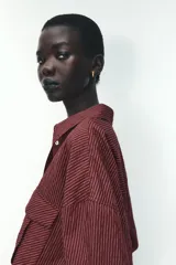 Camisa color borgoña a rayas verticales finas, de corte recto, con cuello solapa y manga larga. Tiene dos bolsillos de parche con solapa en el pecho y cierre frontal con botones.