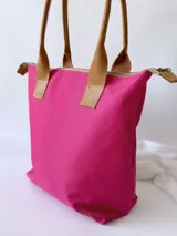 Bolso tipo tote de lona color fucsia con asas de cuero marrón, bolsillo interno y externo.
