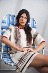 Vestido corto tejido color crudo con rayas verticales marrones y celestes. Tiene cuello redondo y mangas cortas con terminaciones en color rojo.