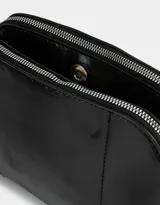 Bandolera negra de cuerina con doble compartimento con cierre y charm lateral. Tiene correa regulable y desmontable.