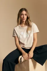 Remera de manga corta color negro con cuello redondo y un aplique bordado de flores y hojas en color beige claro en el centro del pecho.