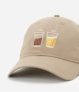 Gorra de sarga color beige con ala curva y hebilla ajustable. Presenta un bordado frontal con dos vasos y las inscripciones '7am' y '7pm'.