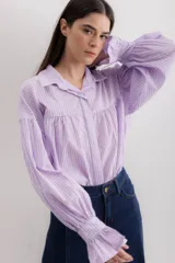Camisa gris a rayas verticales blancas, de corte amplio, cuello alto con lazo y mangas largas abullonadas con puños elásticos.