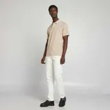 Remera polo color beige de piqué de algodón, con cuello clásico con borde blanco, tapeta de dos botones y mangas cortas con borde blanco.