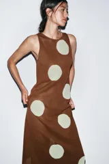 Vestido midi de tejido de punto color marrón, sin mangas y con cuello redondo. Presenta un estampado de lunares grandes en color crema/blanco roto.