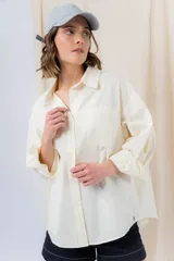 Camisa color crema de algodón liviano, calce oversize, con cuello camisero, cierre abotonado, mangas largas con opción de arremangado y dos bolsillos frontales con solapa.