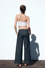 Pantalón culotte de tiro alto en denim azul oscuro, con pernera ancha y corta terminada en vuelta. Presenta falsos botones dorados en la parte delantera, bolsillos frontales y cierre con cremallera y gancho.