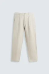 Pantalón de lino color beige, de corte recto, con bolsillos laterales y traseros. Se ajusta a la cintura con cinturón de cuero marrón.