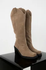 Bota de caña alta color beige, de cuero gamuzado, con taco cuadrado y punta cuadrada.