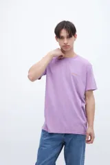 Remera de manga corta color lila con cuello redondo y parche con texto en el pecho.