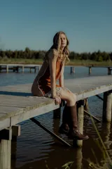 Vestido corto marrón de gamuza sintética, sin mangas, con escote en V y detalle de flecos en el ruedo. Presenta apliques bordados en el frente y laterales.