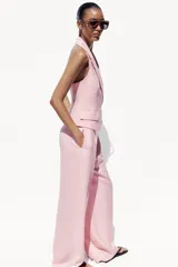Chaleco rosa con cuello halter y escote pico con solapa. Espalda descubierta. Bolsillos delanteros con solapa. Cierre frontal cruzado con botones.
