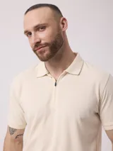 Remera tipo polo color beige, de manga corta y corte clásico, con cierre parcial frontal con cremallera.