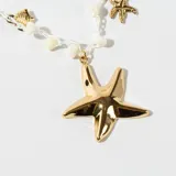 Collar corto con cadena de hilo blanco, cuentas de plástico color crema y dijes colgantes de metal dorado con forma de pez y estrellas de mar.