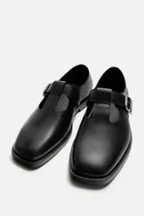 Zapato tipo Mary Jane de cuero negro con hebilla lateral, horma redonda y suela con ligero tacón.